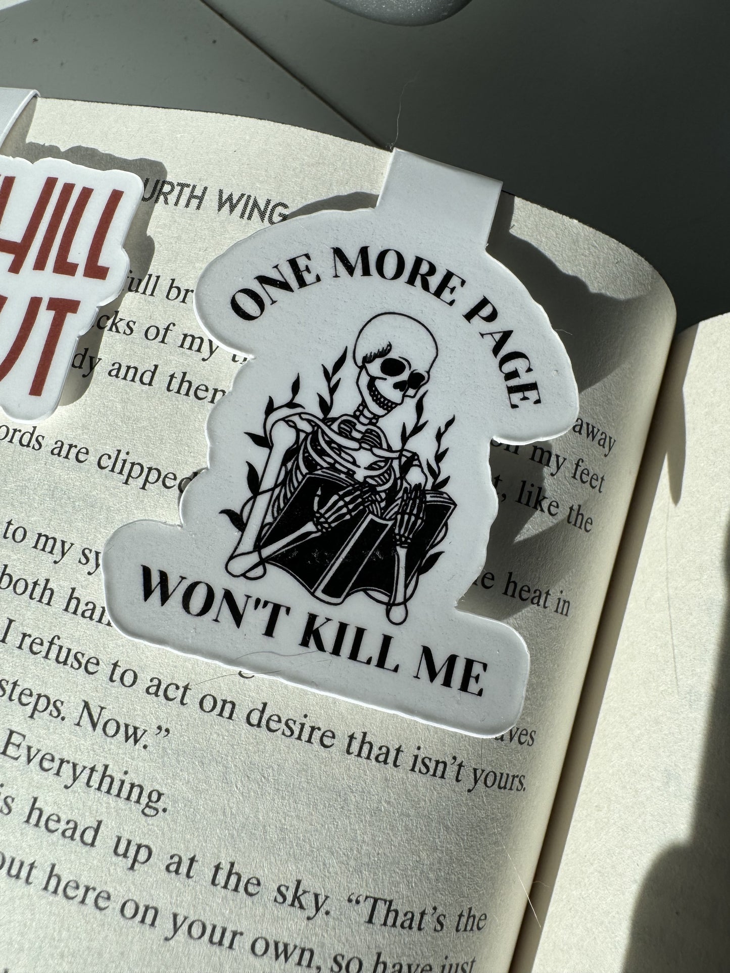 "One More Page Won't Kill Me' magnetic bookmark with a skeleton reading a book