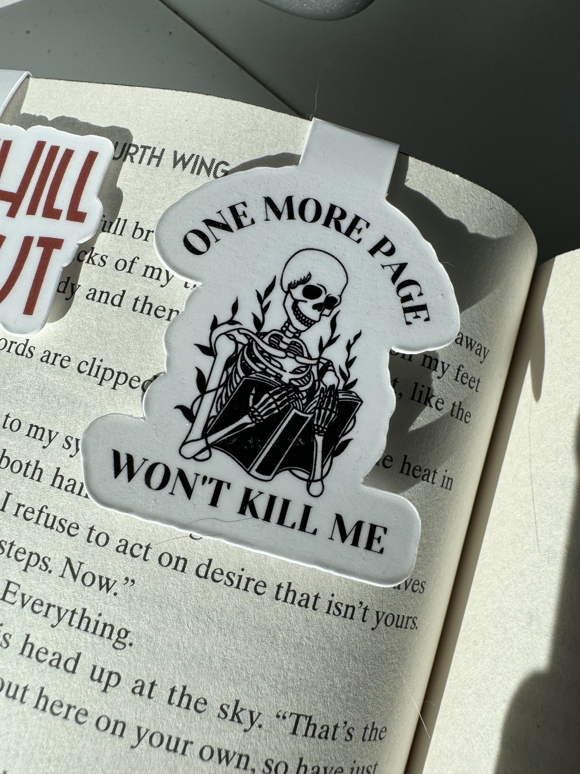 "One More Page Won't Kill Me' magnetic bookmark with a skeleton reading a book